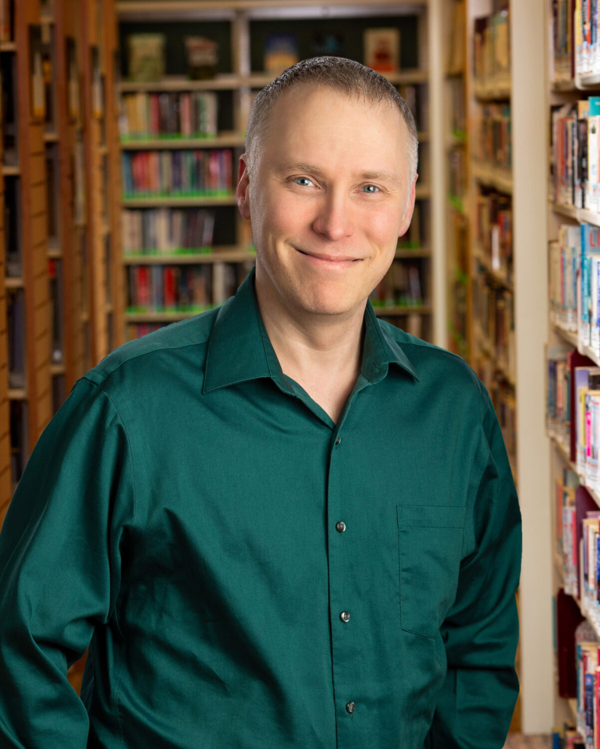 smiling man in a green shirt stands in front of library shelves