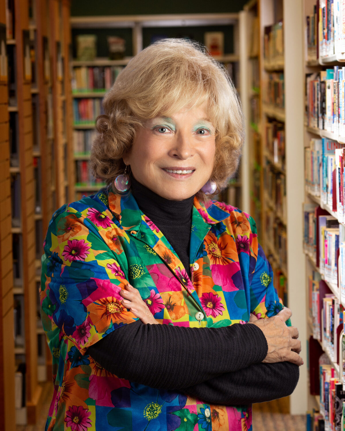 Woman in brightly colored shirt smiles with arms crossed