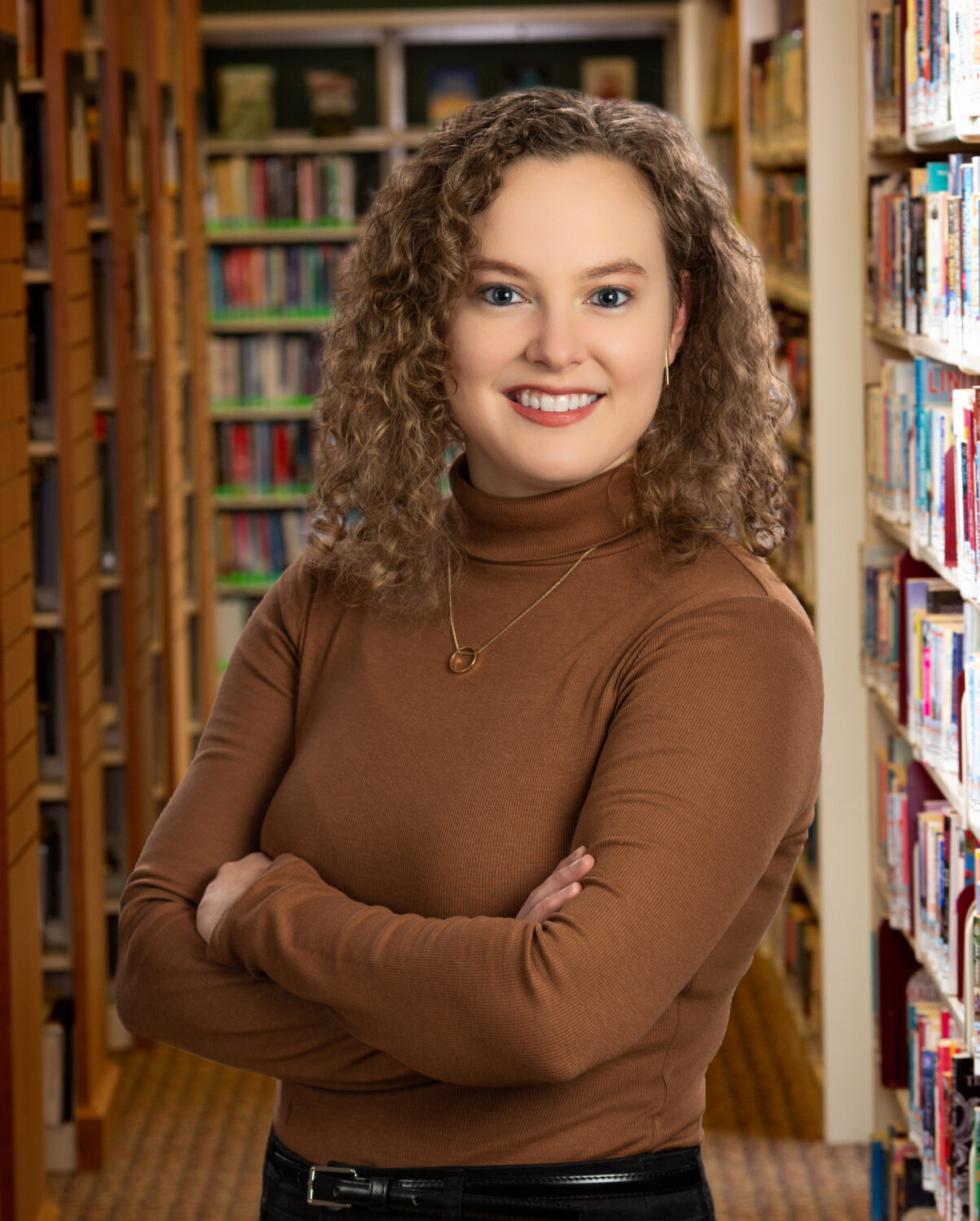 woman in turtleneck sweater smiles at camera with arms crossed