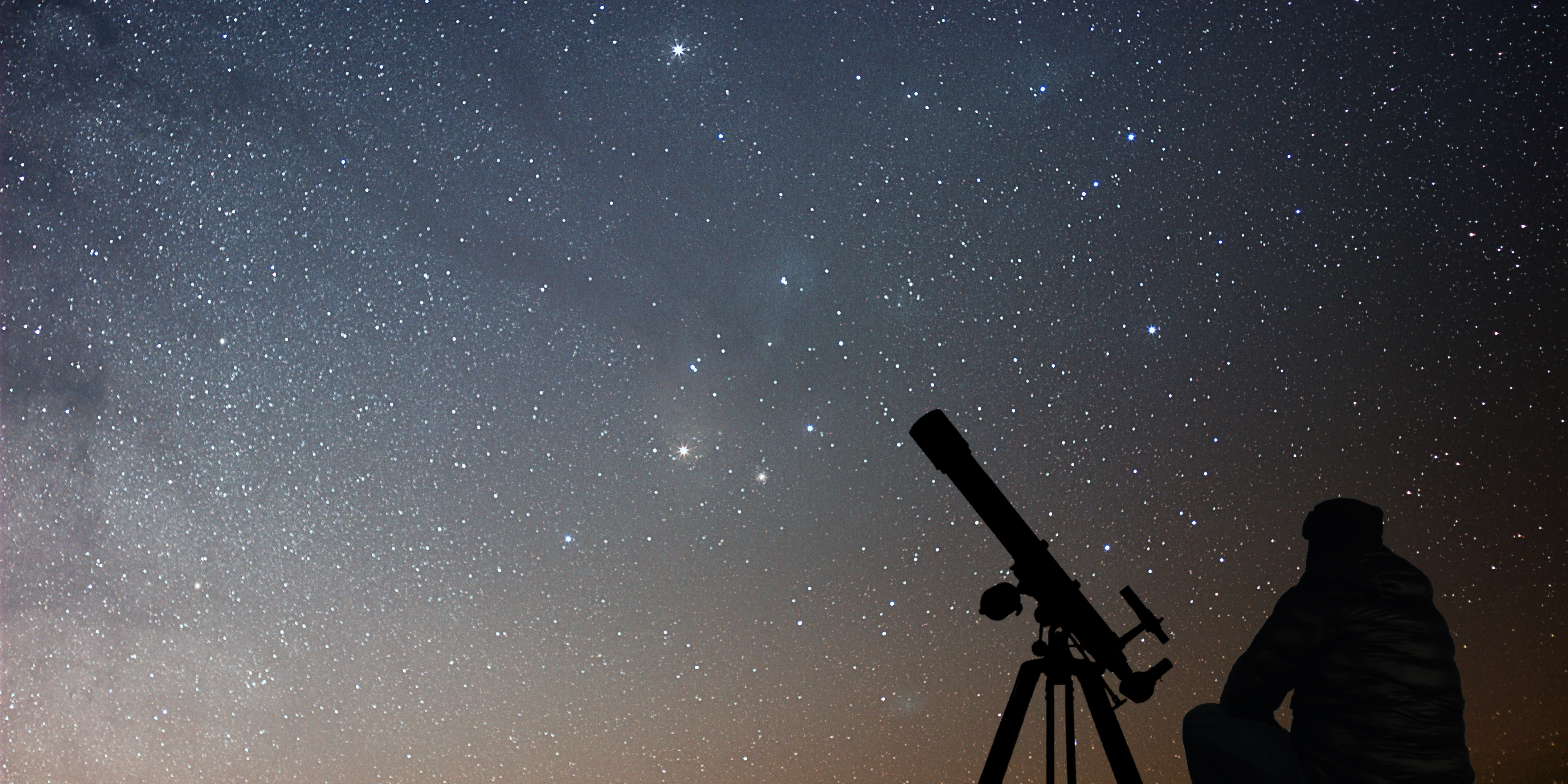 person sitting next to a telescope with a starry sky in the background