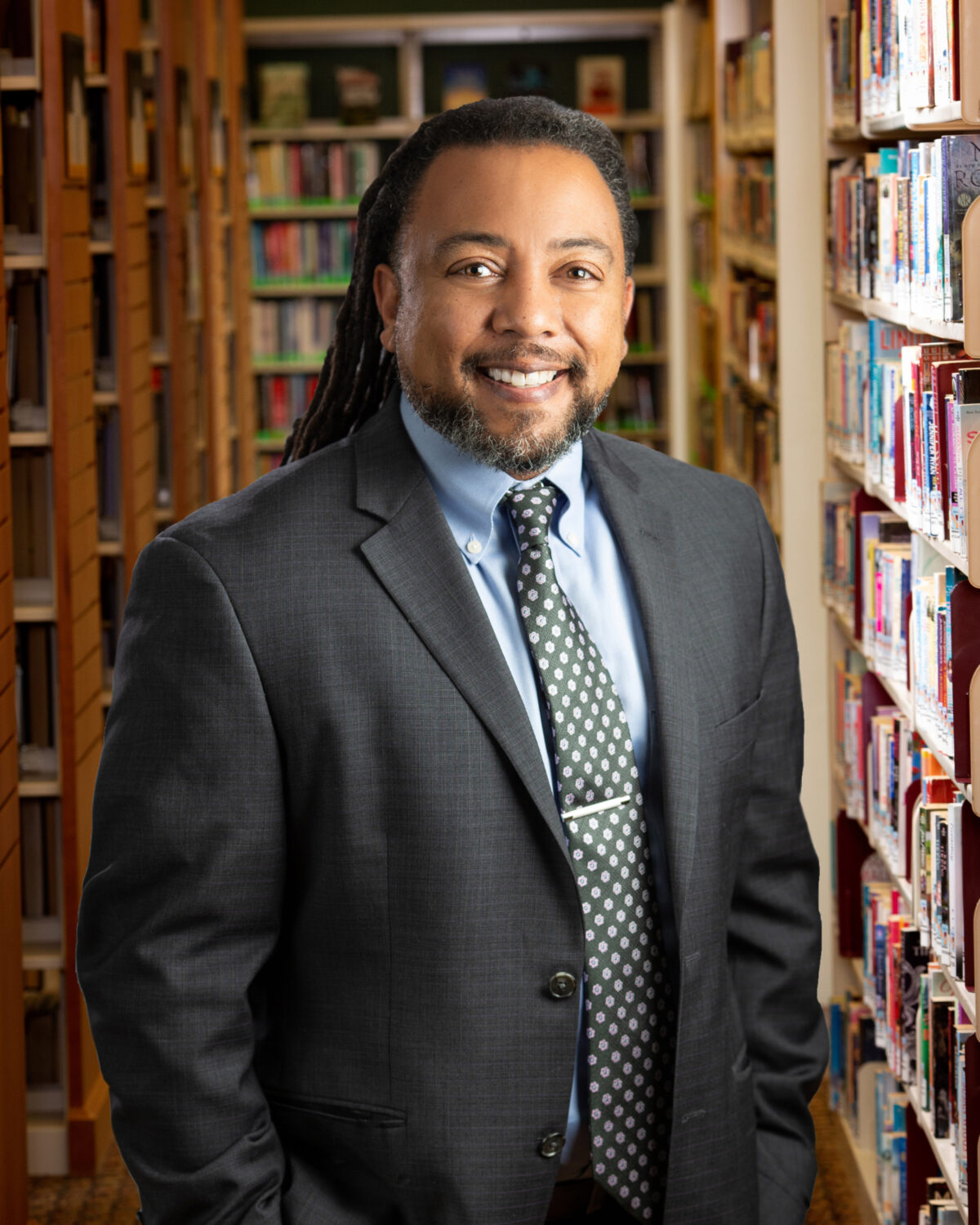 Man with jacket and tie stands in front of book shelves