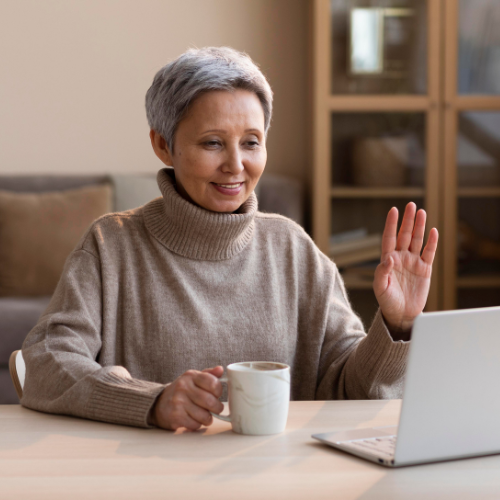 woman with white hair waving to a computer screen with a mug in her hand