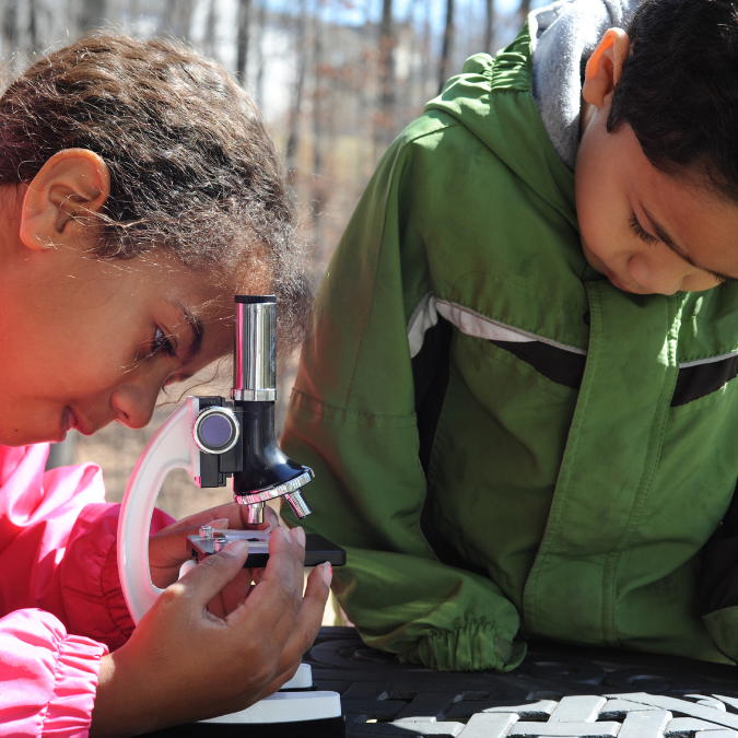 two children play with a microscope outdoors