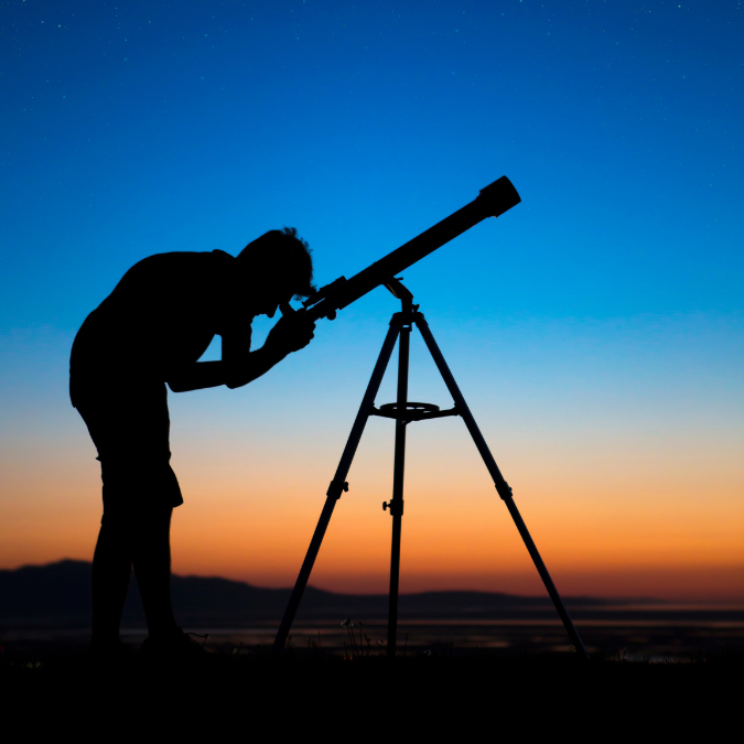 An outline of a person looking through a telescope with the sun setting in the background