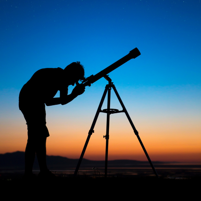 silhouette of person using a telescope at dusk