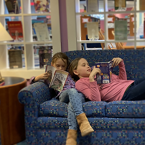 tween girls read together on couch