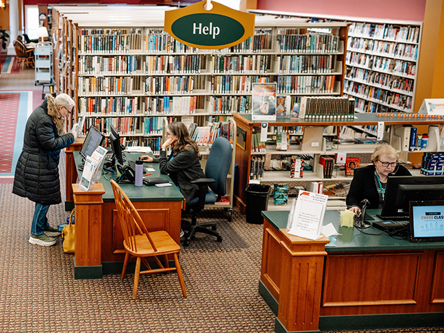 librarians at desk offer readers' advisory service to woman and on phone
