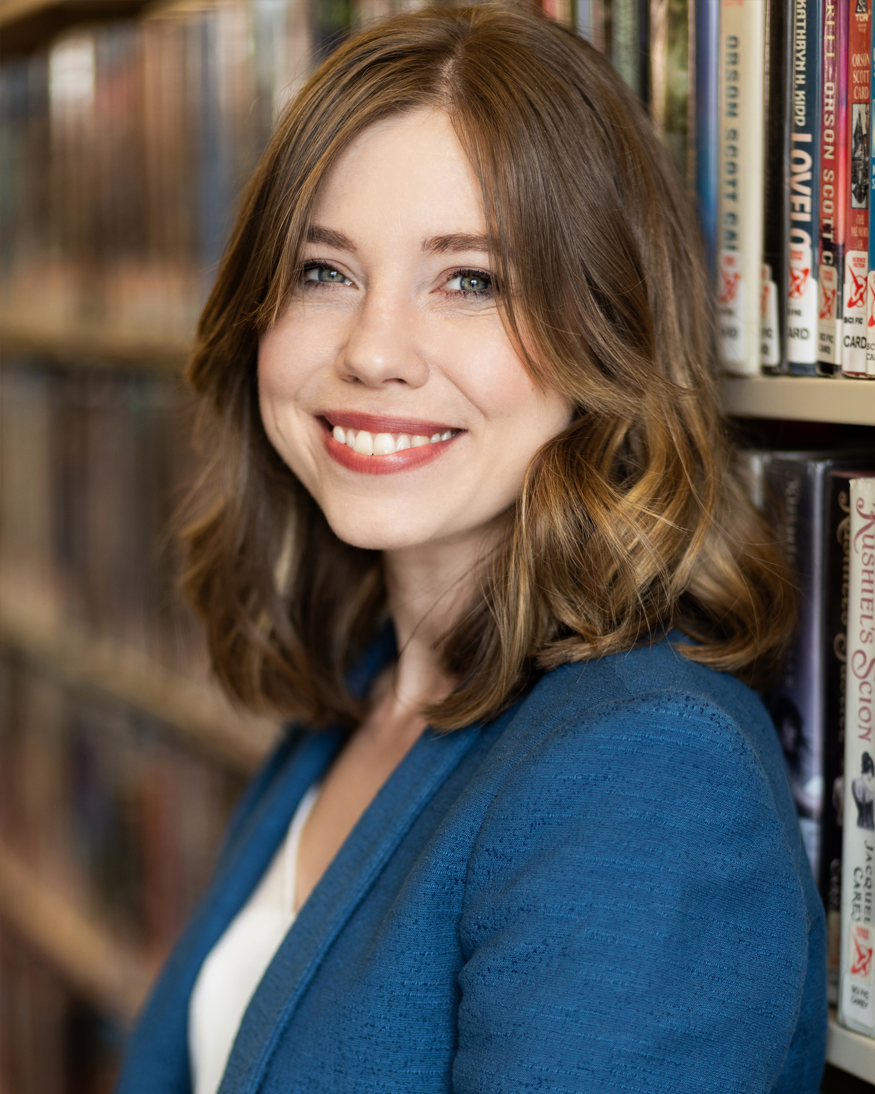 smiling woman leans against a book shelf