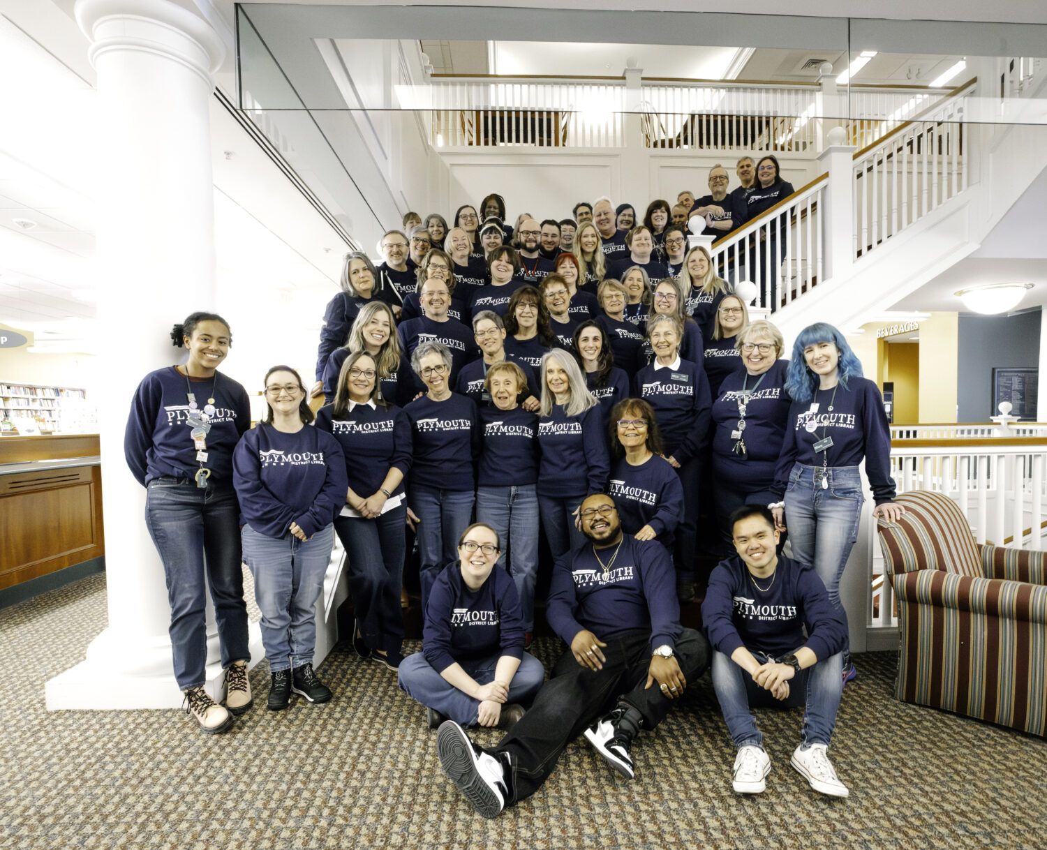 a group of smiling library employees standing on the library staircase