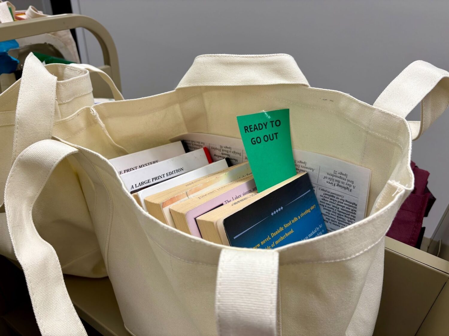 A white tote bag containing books with a green slip that reads "Ready to Go Out".