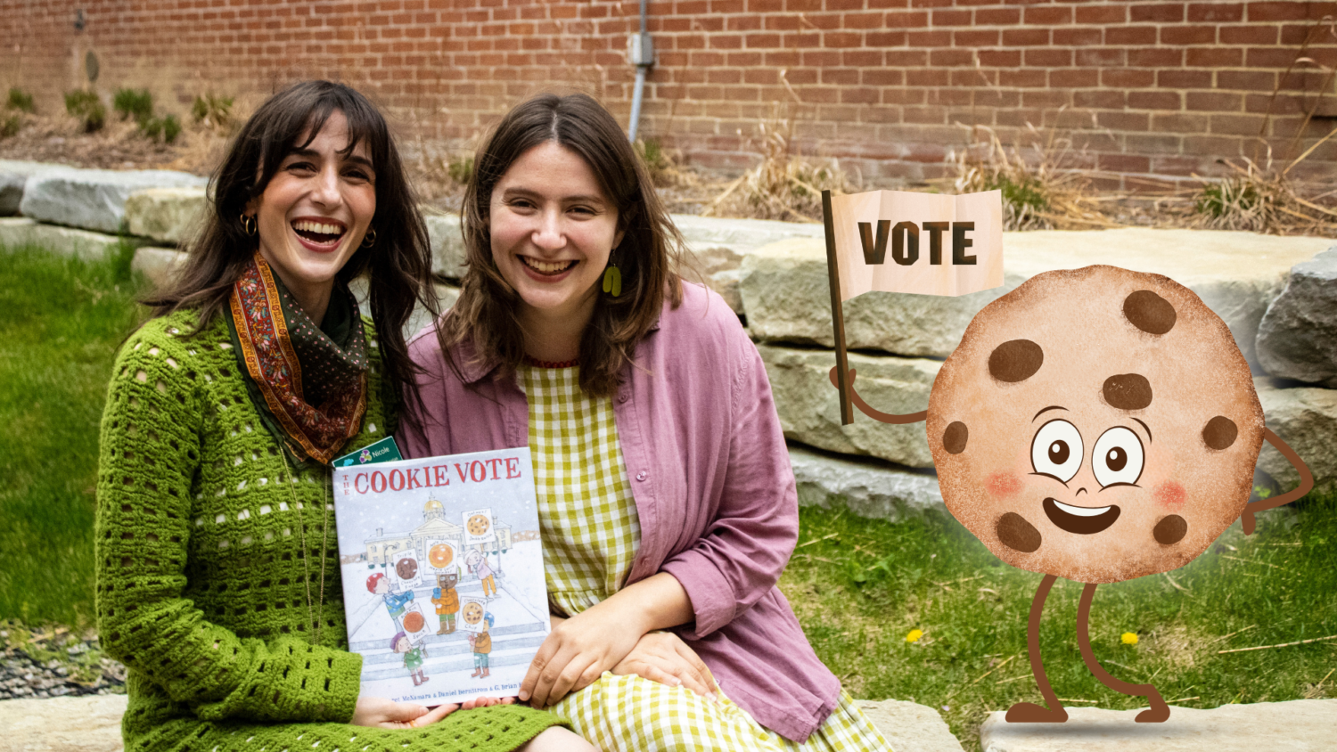 Two librarians pose with a copy of The Cookie Vote outside with a brick wall behind them. A watercolor cookie holding a flag that says "Vote" smiles beside them.