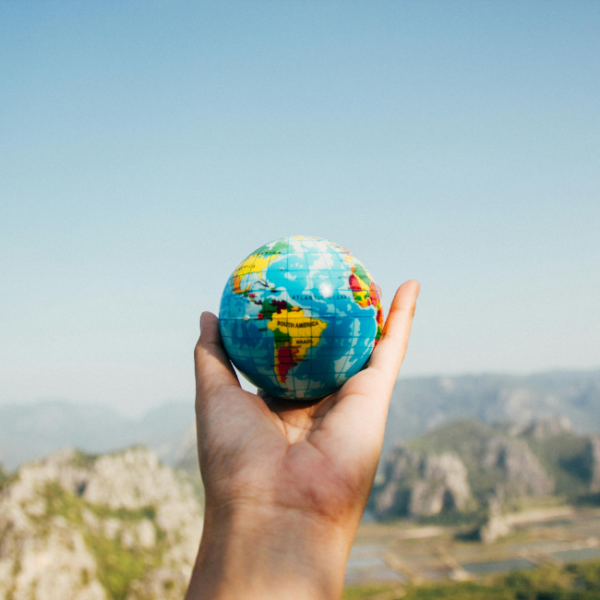 A hand holds a globe outdoors under the blue sky.