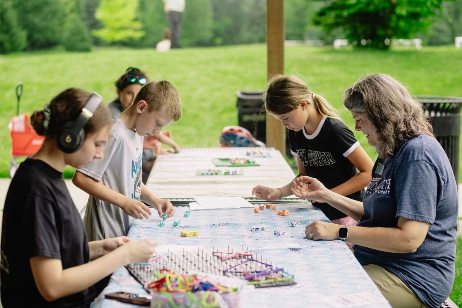 5 Plymouth community members sit at a table playing a board game with dice.