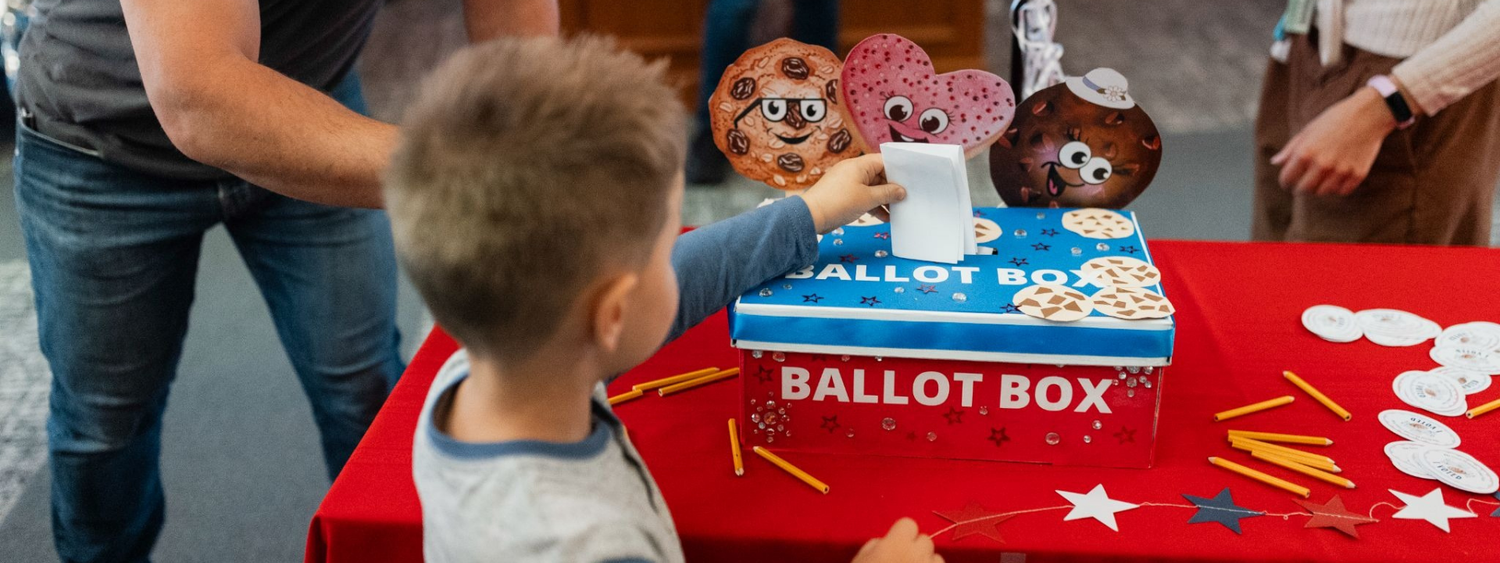 A young boy places his ballot in the Official Plymouth Cookie Vote ballot box.