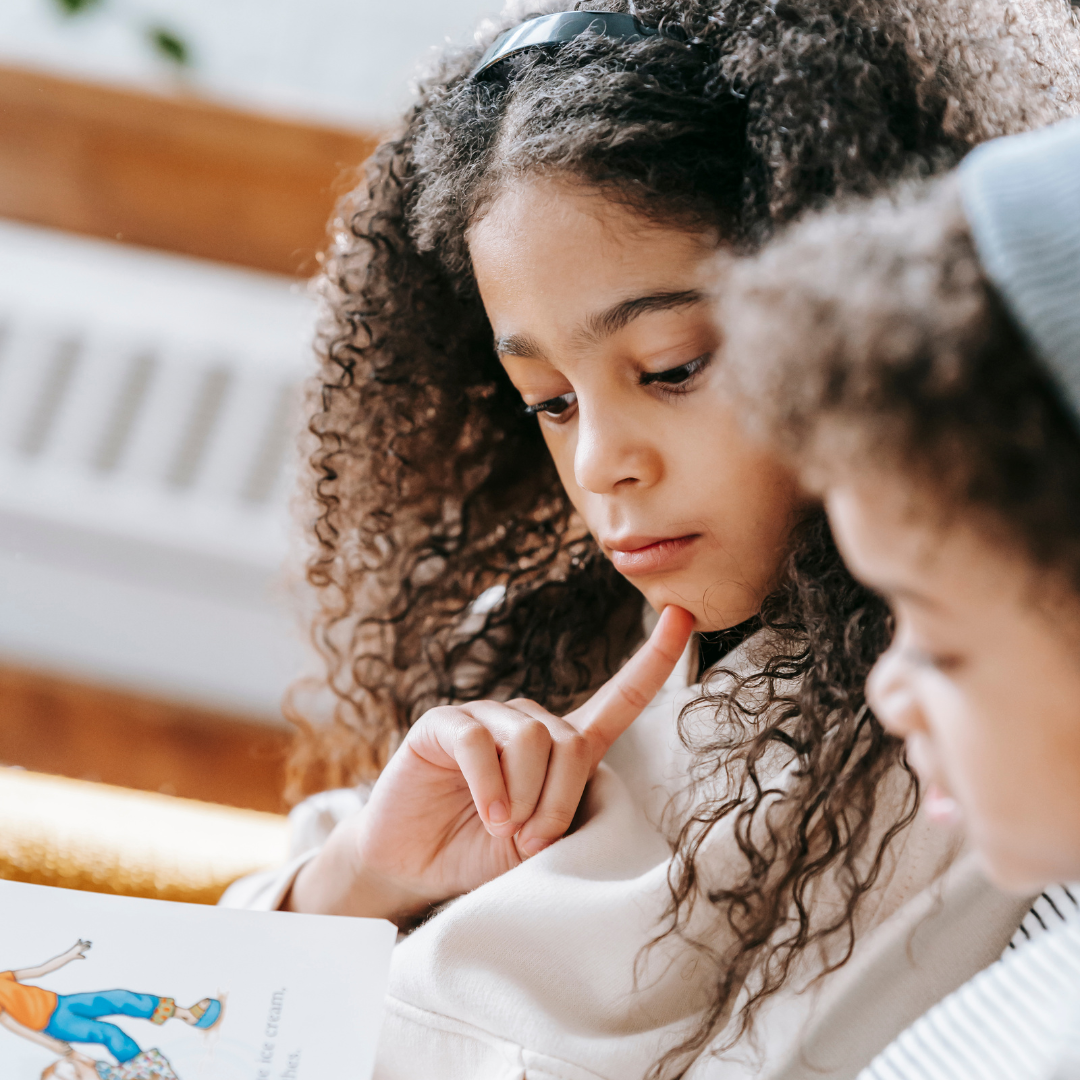 a young girl reads to her little brother