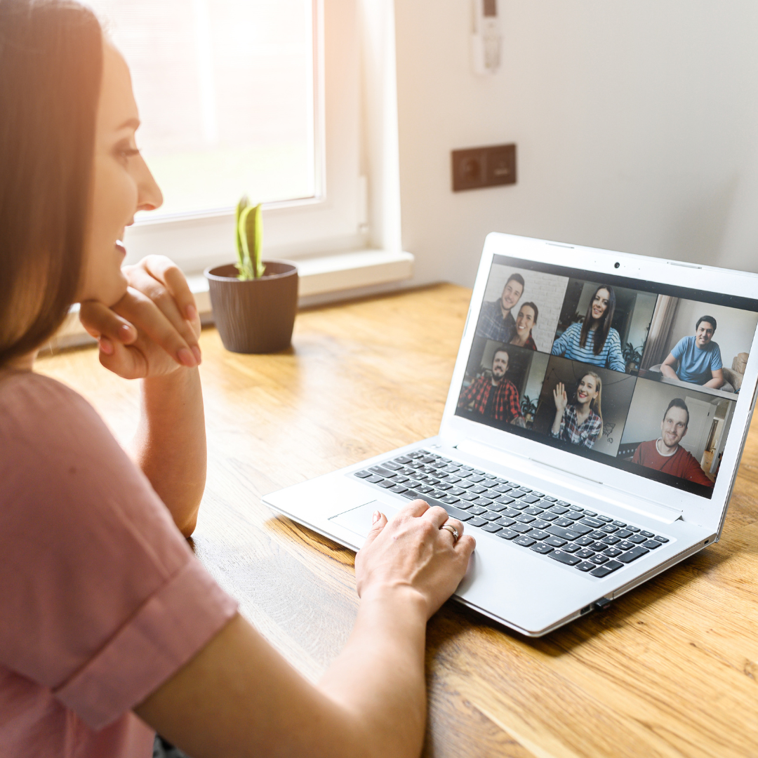 a woman sits at a computer. the screen shows 6 people on a video call.