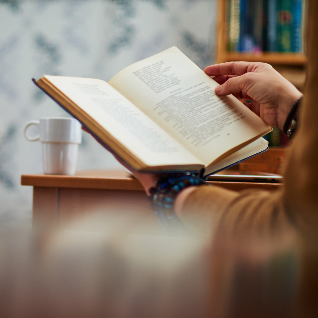 two hands hold open a book with a cup of coffee resting nearby.