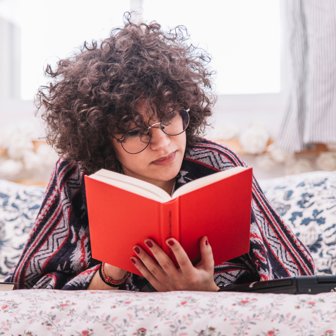 young person with curly hair reading a book with a red cover